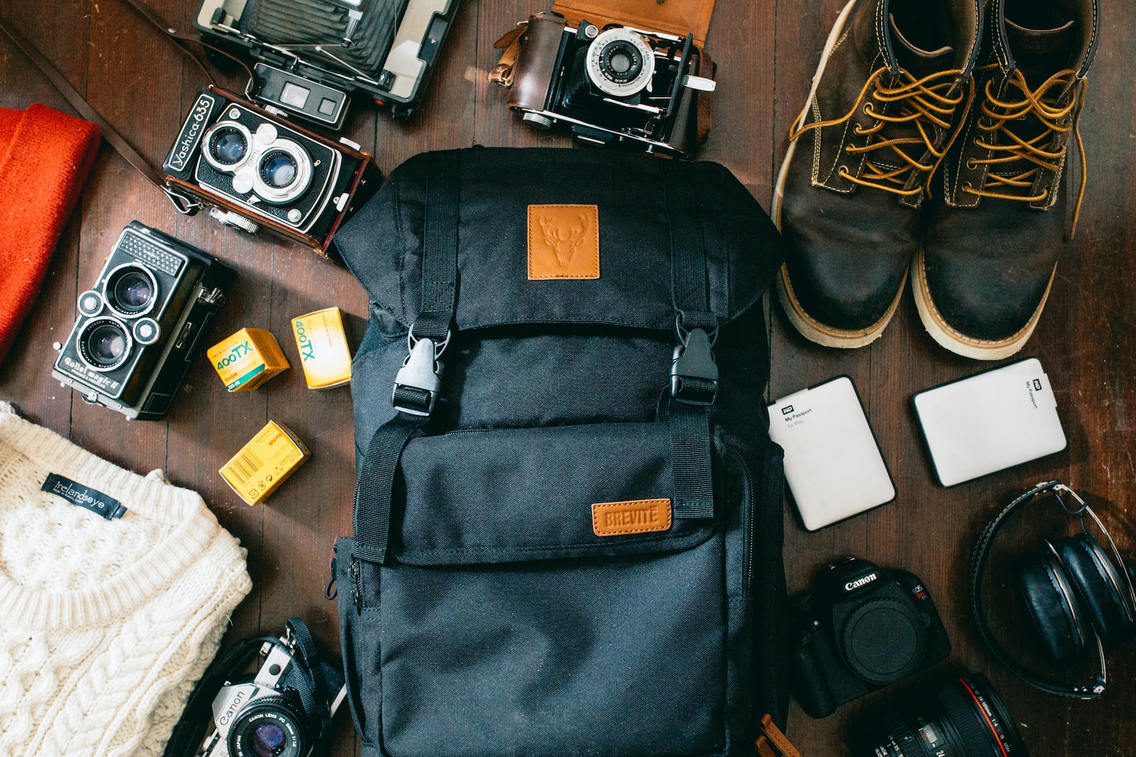 high-angle photo of black bag beside cameras, portable HDD and black leather lace-up boots