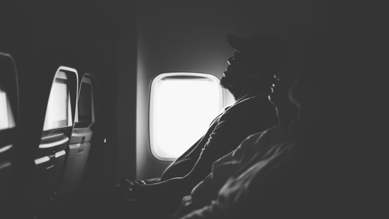 grayscale photo of three person sitting inside airplane