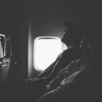 grayscale photo of three person sitting inside airplane