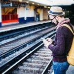 man using phone while standing in front of train rail during daytime