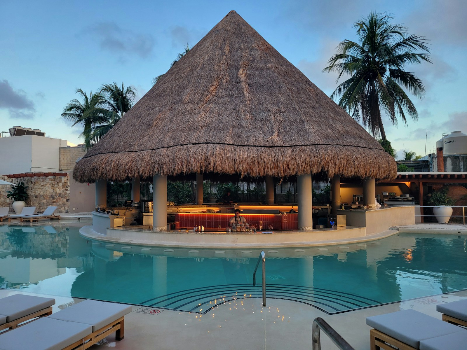A pool with a thatched roof and lounge chairs