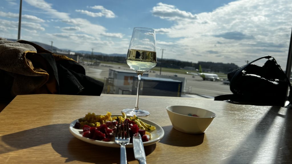 Un verre de vin et une petite salade dans un salon d'aéroport à Zürich avec une vue sur le tarmac