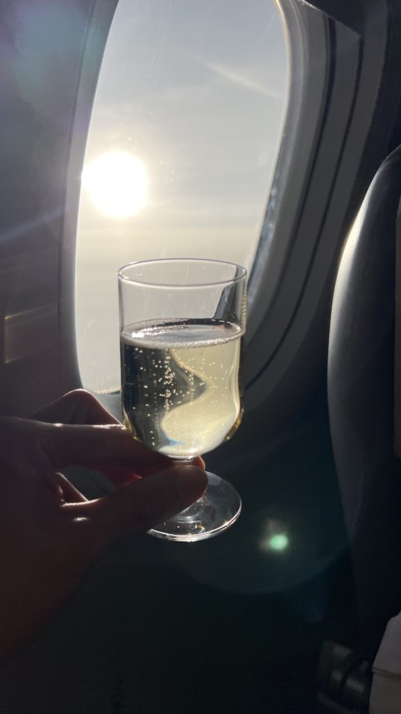 Un verre de mousseux dans un avion avec en arrière-plan un hublot