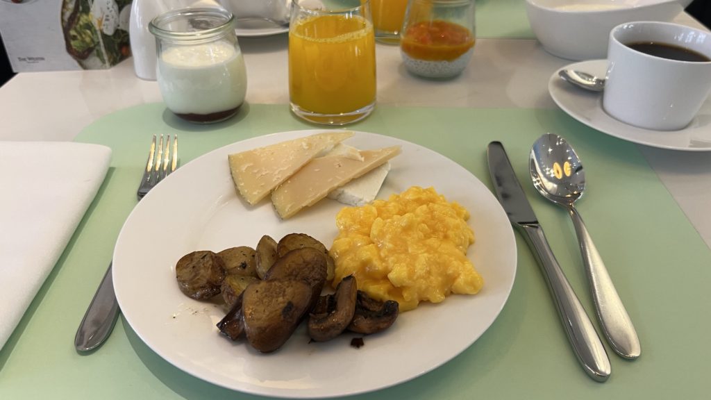 Une assiette de petit-déjeuner composée de fromage, d’œufs, de pommes de terres et d'un café
