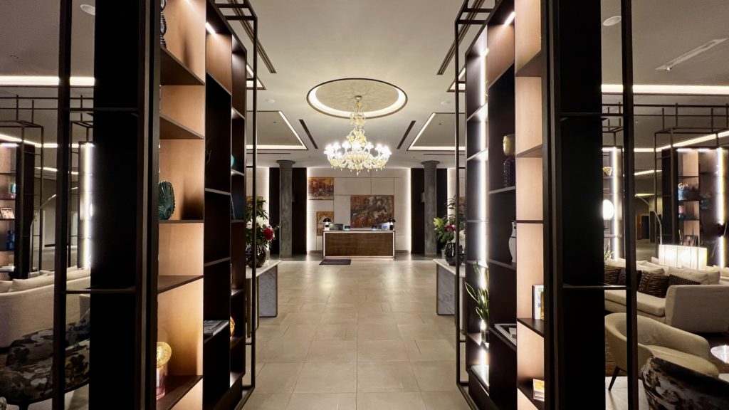 Un hall d'entrée dans un hôtel avec des étagères sur le côté, un lustre central et un comptoir d'enregistrement en fond